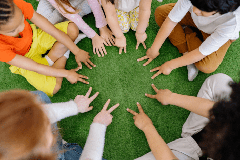 children laying hands on a green grass circle